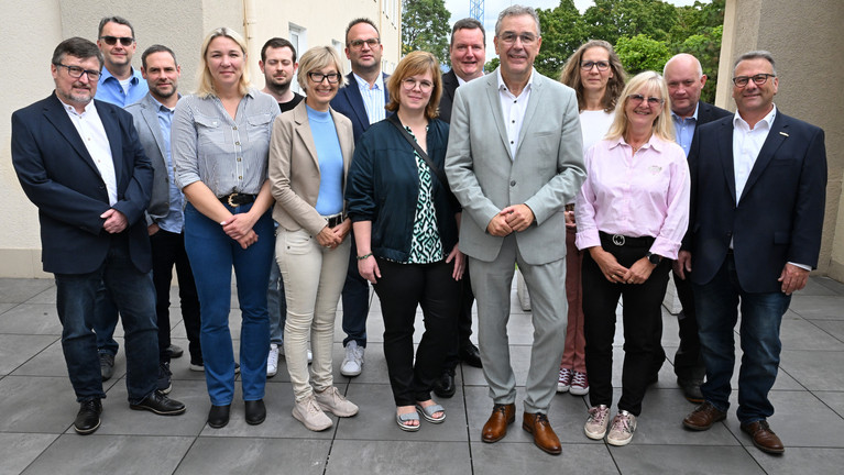 Gruppenfoto von 14 Personen, die draußen vor einem Gebäude zusammenstehen.